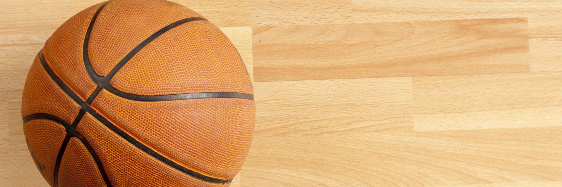 A basketball on a light wooden court, positioned on the left side of the image.