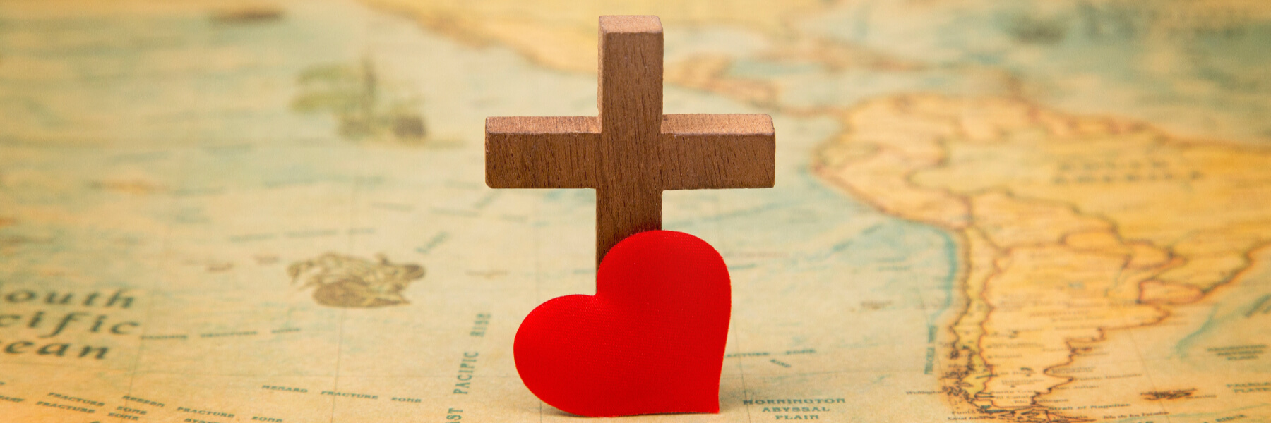 A wooden cross and a red heart placed on a map showing part of South America and the Pacific Ocean.