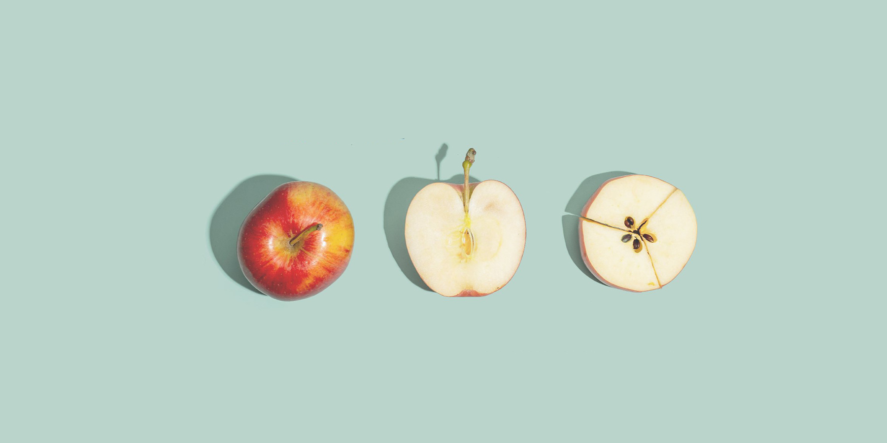 A whole apple, a vertically sliced apple half, and a horizontally sliced apple half are arranged in a row on a pale blue background.